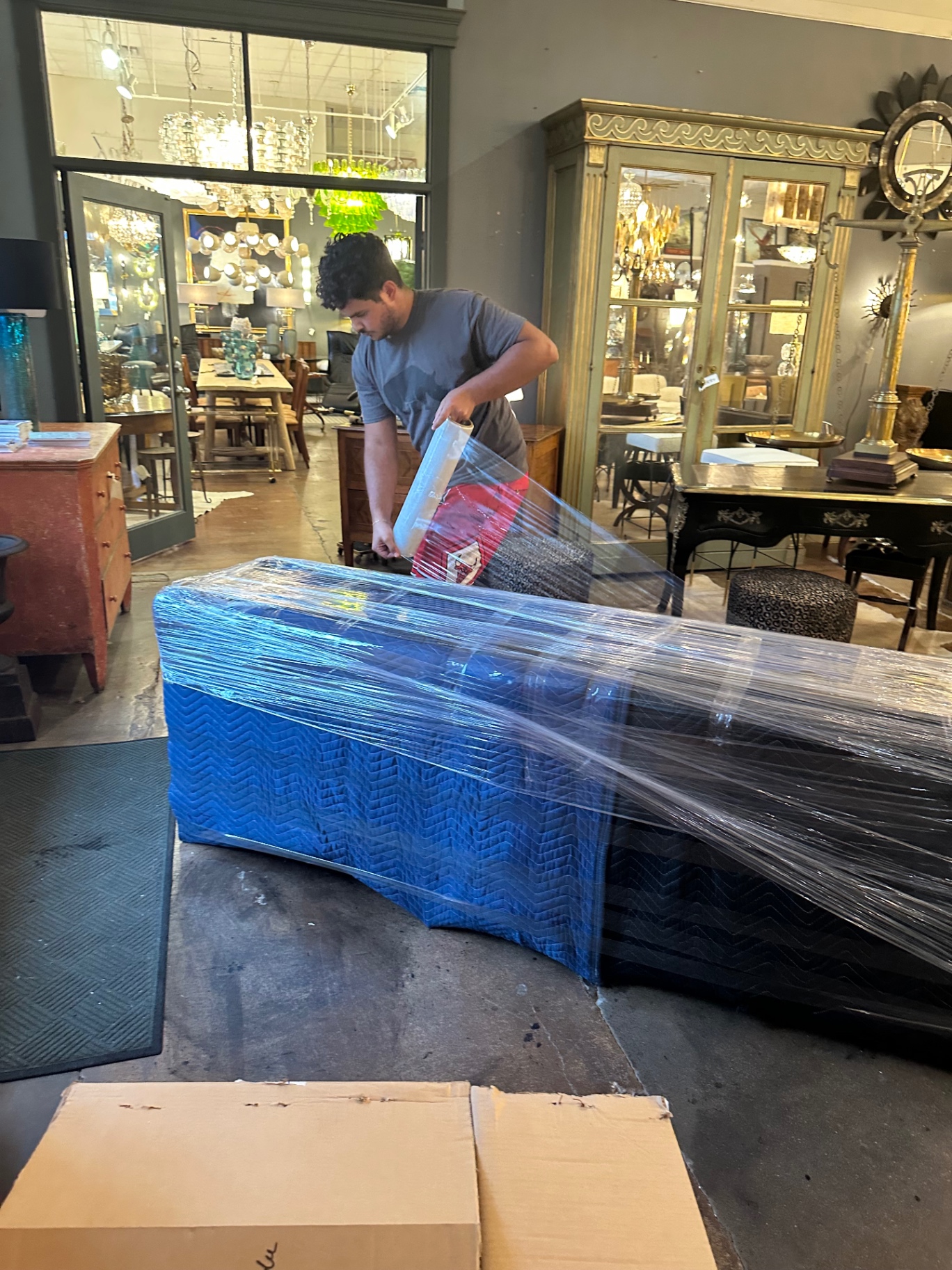 Mover wrapping an antique piece of furniture in blue moving pads and stretch wrap at a showroom