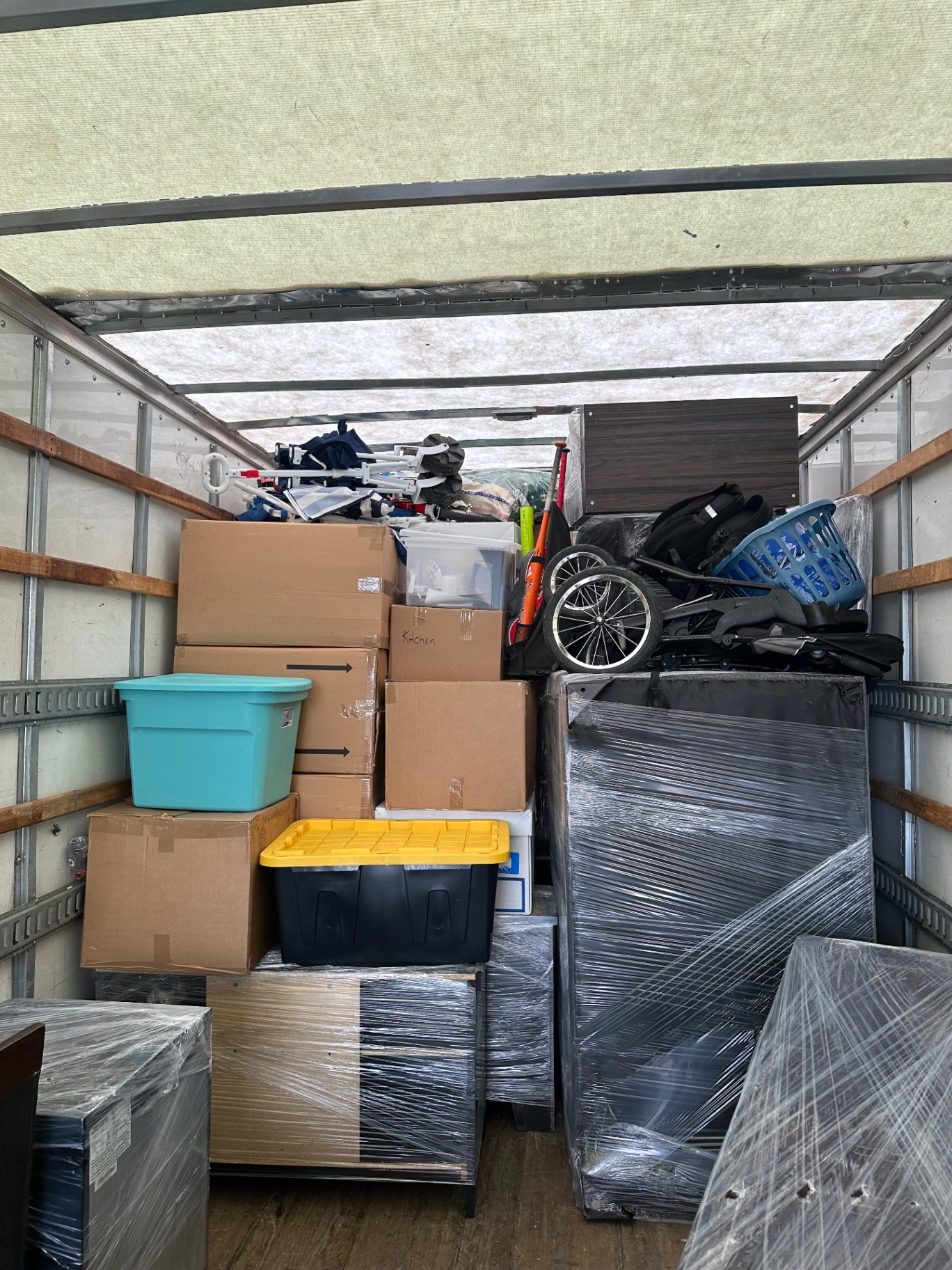 Interior of a moving truck packed floor-to-ceiling with boxes, storage bins, and shrink-wrapped furniture